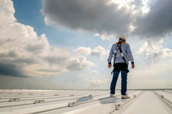 Man on roof wearing safety gear performing a roofing maintenance inspection