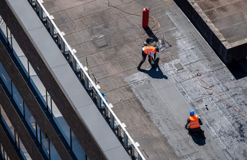 A team of roofing professionals performs a repair on an industrial roof.