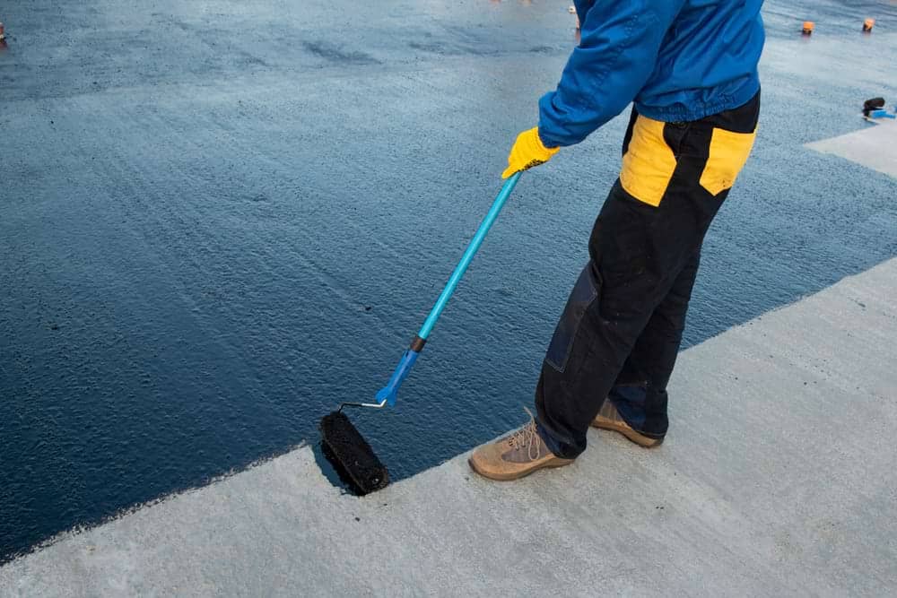 A roofing technician applies a liquid roofing sealant on a commercial rooftop