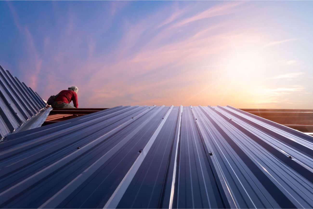 A contractor installs metal roofing panels on a commercial flat roof at sunset.